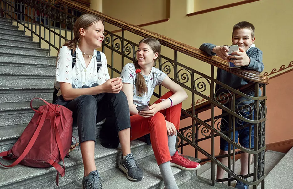 Oppilaat Minttu Sahlström, Lotta Forsström ja Oiva Riihelä istuvat koulun portaikossa kertomassa Atea Smart School -kännykkäsovelluksen käytöstä.
