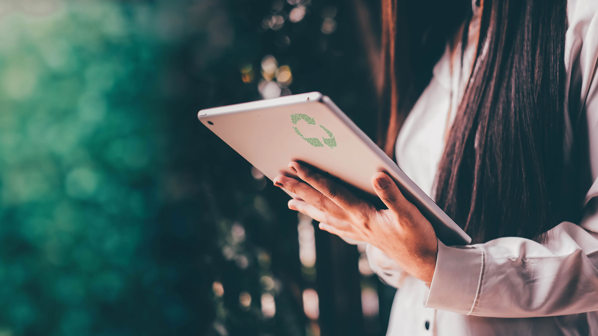 Pitkähiuksinen nainen pitää kädessään tablettitietokonetta, jonka takakannessa on kierrätyssymboli.