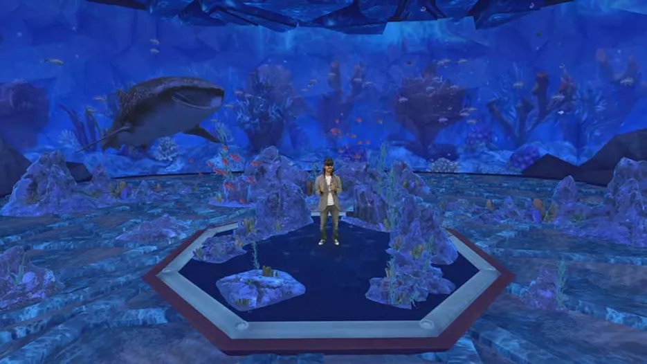 Microsoftin Alex Kipman seisoo keskellä merenpohjaa Mesh-virtuaalisovelluksessa. Ympärillä näkyy koralleja ja takana ui hai.