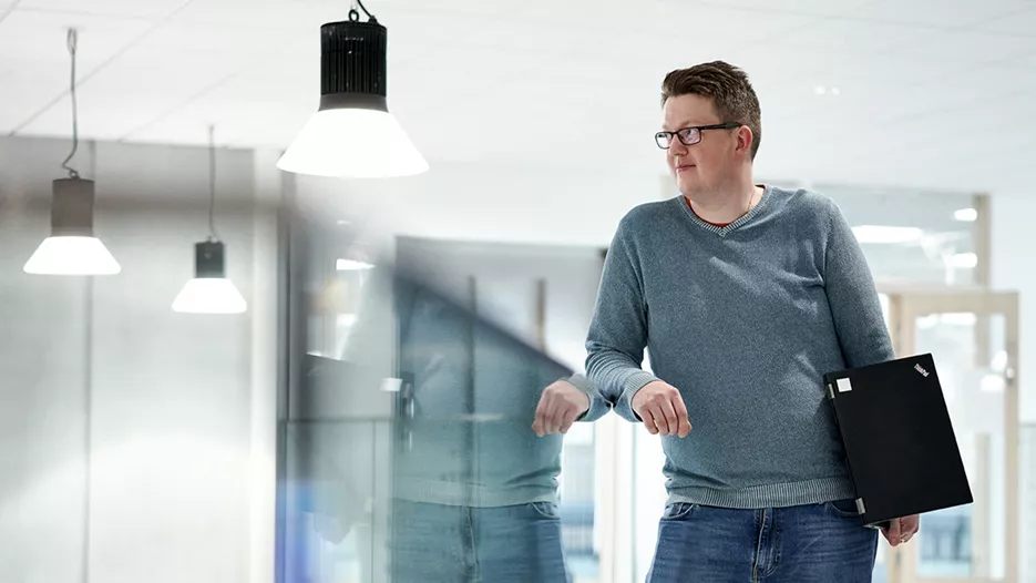 Tiera Verkkokauppa referenssi, Parkanon Kaarna koulukampus: Mies, jolla on silmälasit seisoo nojaten lasikaiteeseen. Hänellä on kannettava tietokone kainalossa.