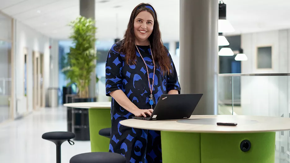 Tiera Verkkokauppa referenssi Parkanon Kaarna koulukampus. Nainen sini-mustassa vaatteessa nojaa pöytään ja käyttää tietokonetta samalla.