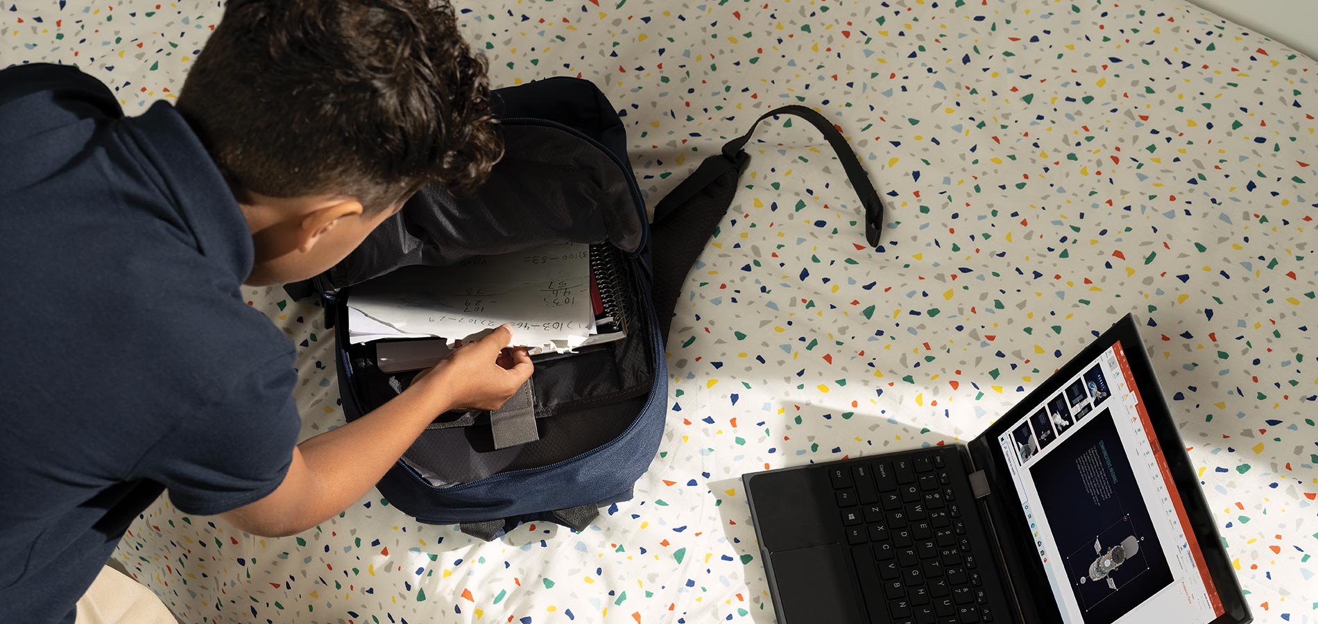 Poika pakkaa reppua, tietokone esillä tasolla.