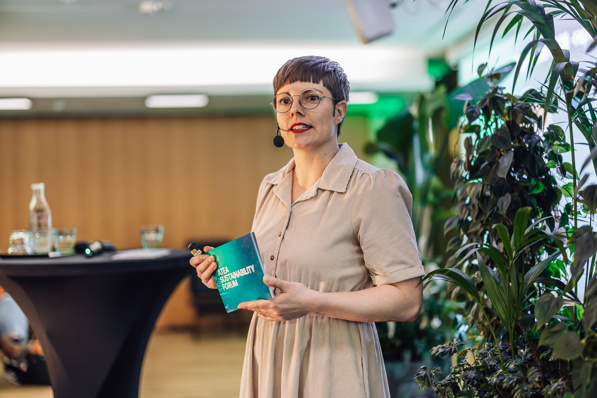Atean vastuullisuuspäällikkö Elli Ojala seisoo puhujanpöydän edessä, hänellä on käsissään kortteja, joissa lukee Atea Sustainability Forum.