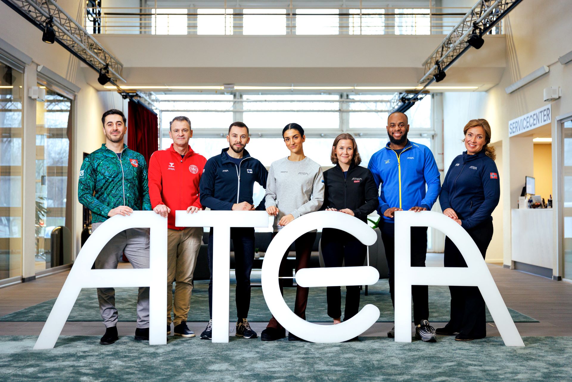 Seitsemän eri Atea-maita edustavaa henkilöä seisoo ATEA-kirjainten takana.